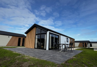 Moderne Lodge Velthorst auf den IJssel-Inseln in den Niederlanden mit Terrasse und Gartenmöbeln bei blauem Himmel.