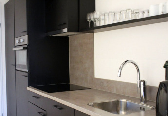 Cuisine de tiny house moderne avec placards noirs, évier, four, plaques et verres sur étagère aux Pays-Bas.