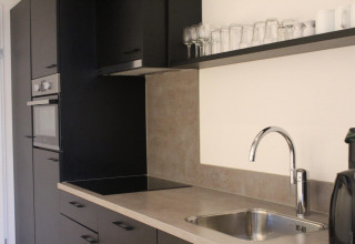 Cucina moderna di tiny house con mobili neri, forno, piano cottura, lavello e bicchieri su mensola in Olanda.