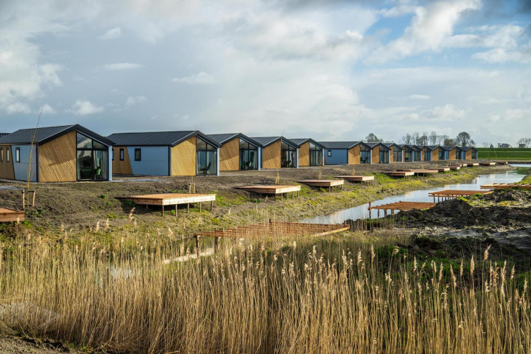 Rangée de tiny houses modernes au bord de l'eau aux Îles IJssel, Pays-Bas, sous un ciel partiellement nuageux.
