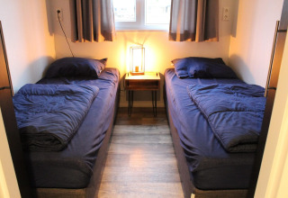 Zwei Einzelbetten mit dunkelblauer Bettwäsche in einem kleinen Zimmer im Tiny House Berkel, IJsselinseln, Niederlande.