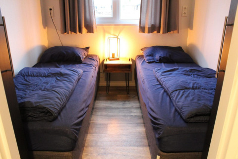 Due letti singoli con biancheria blu scuro in una piccola stanza della tiny house Berkel alle Isole IJssel, Paesi Bassi.