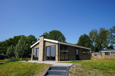 Buitenzicht op Hackfort-lodge op een zonnige dag met gazon voor en bomen op de achtergrond.