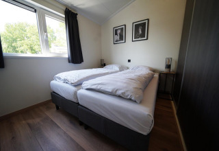 Moderne lodge-soveværelse på Hackfort, IJssel Islands, Nederlandene, med to enkeltsenge og stort vindue.