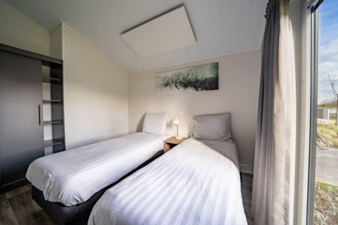 Habitación luminosa con dos camas, mesita, arte y ventana grande en Hackfort Lodge, Islas IJssel, Países Bajos.