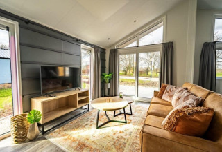 Lyst og moderne opholdsstue i Hackfort-lodge på IJssel-øerne, Holland, med sofa og udsigt til haven.