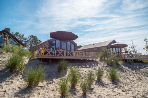 Outdoor view of Solo Retreat lodge with people relaxing on the deck among sandy dunes and patio umbrellas.