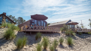 Udendørs udsigt over Solo Retreat lodge med familier, der nyder terrassen på sandede klitter under paraply.