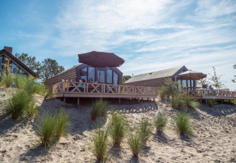 Outdoor view of Solo Retreat lodge with people relaxing on the deck among sandy dunes and patio umbrellas.