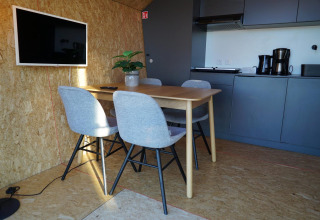 Interior moderno en Solo Retreat en las Islas IJssel, Países Bajos, con mesa, cuatro sillas y cocina pequeña.