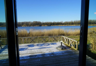 Vista da un lodge al Solo Retreat alle Isole IJssel, Paesi Bassi, con terrazza e paesaggio sull'acqua.