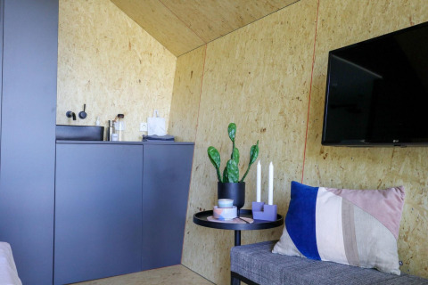 Modern lodge-interieur in Solo Retreat, IJssel Islands, met kitchenette, plant, kaarsen en wand-tv.