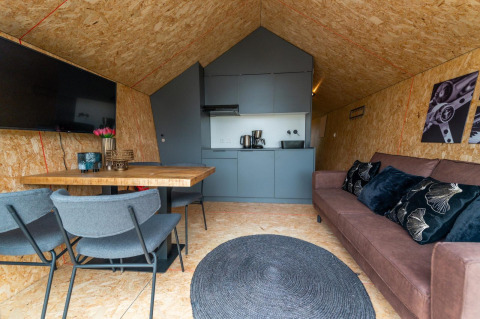 Interior view of Solo Retreat lodge at The IJssel Islands, Netherlands, featuring sofa, kitchen, and TV.