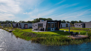 Moderne Just Nature-lodges aan het water met grasveld, terras en omringd door natuur.