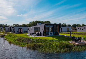 Moderne Just Nature Lodges am Seeufer mit Grünfläche, Terrasse und Wasser bei sonnigem Wetter.