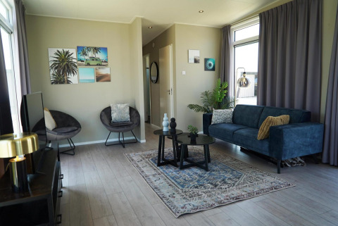 Sala de estar en Just Nature lodge en las Islas IJssel con sofá azul, sillones, alfombra y grandes ventanas.