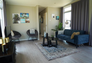 Woonkamer in Just Nature lodge bij de IJssel-eilanden met blauwe zetel, fauteuils en ramen met gordijnen.