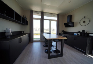 Moderne keukenlodge aan de IJssel Eilanden, Nederland, met zwarte kasten, houten tafel en grote ramen.
