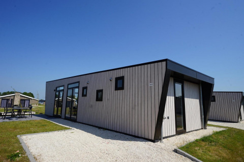 Lodge moderne à Just Nature, Îles IJssel, aux Pays-Bas, avec ciel bleu et espace extérieur pour s’asseoir.