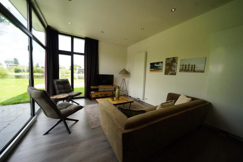 Modernes Wohnzimmer in der L-Cube Lodge Spaarnwoude, Niederlande, mit Panoramafenstern und Gartenblick.