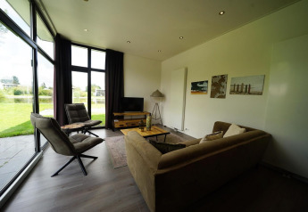Moderne lounge i L-Cube Spaarnwoude, Holland, med store vinduer og udsigt til grøn have og sø.
