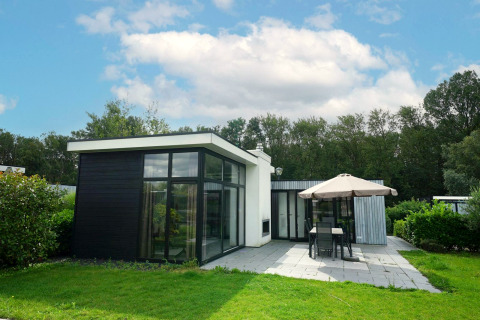 Lodge moderne L-Cube à Spaarnwoude, Pays-Bas, avec de grandes baies vitrées, terrasse et salon de jardin.