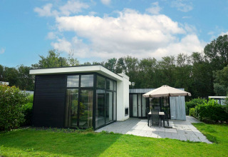 Lodge moderne L-Cube à Spaarnwoude, Pays-Bas, avec de grandes baies vitrées, terrasse et salon de jardin.