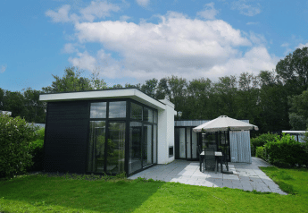Moderne L-Cube lodge in Spaarnwoude, Nederland, met grote ramen, betegeld terras en tuinmeubilair.