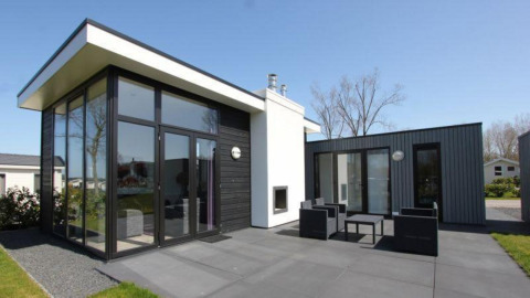Modernes L-Cube-Lodge bei Spaarnwoude, Niederlande, mit großer Glasfassade und gemütlicher Terrasse.