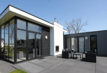 Moderne lodge L-Cube ved Spaarnwoude, Holland, med store vinduer, terrasse og udendørs siddepladser.