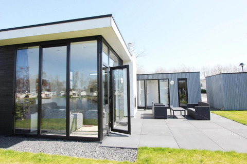 Moderne L-Cube Lodge in Spaarnwoude, Niederlande, mit großen Fenstern, Terrasse und Gartenblick.