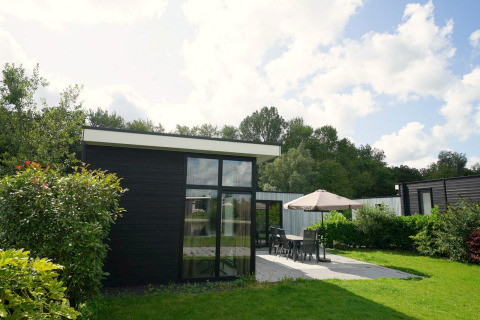 Lodge moderne L-Cube à Spaarnwoude, Pays-Bas, avec terrasse, mobilier de jardin et pelouse verdoyante.