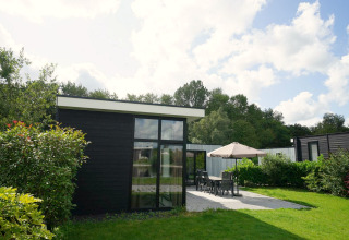 Lodge moderne L-Cube à Spaarnwoude, Pays-Bas, avec terrasse, mobilier de jardin et pelouse verdoyante.