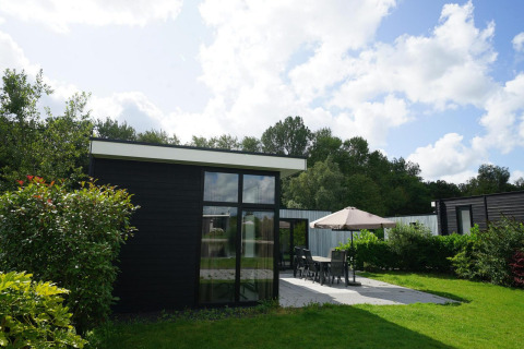 Lodge L-Cube moderno en Spaarnwoude, Países Bajos, con patio, muebles de exterior y jardín verde exuberante.