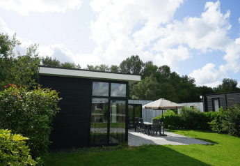 Luxe L-Cube lodge in Spaarnwoude, Nederland, met terras, tuintafel en aantrekkelijke groene tuin in zonlicht.