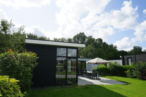 Moderne L-Cube lodge i Spaarnwoude, Holland, med terrasse, havemøbler og grønne omgivelser på en solrig dag.