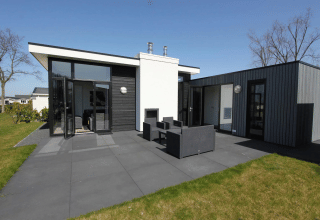 Moderne lodge ved Spaarnwoude, Holland med sort og hvid facade, terrasse og havemøbler under blå himmel.