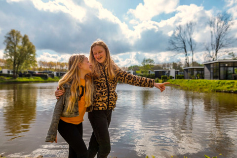 Deux filles souriantes près du lac devant le lodge L-Cube à Spaarnwoude, Pays-Bas, par une journée ensoleillée.