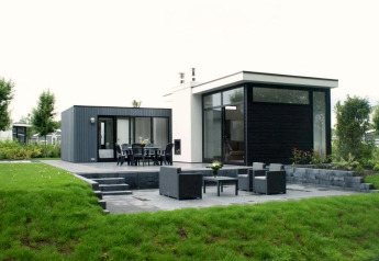 Moderna cabaña L-Cube con amplia terraza, muebles de exterior y jardín verde en entorno tranquilo.