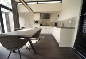 Zona de comedor y cocina moderna en la cabaña L-Cube en Spaarnwoude, Países Bajos, con diseño elegante y ventanas.