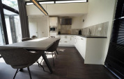 Zona de comedor y cocina moderna en la cabaña L-Cube en Spaarnwoude, Países Bajos, con diseño elegante y ventanas.