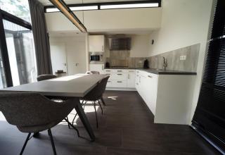 Zona de comedor y cocina moderna en la cabaña L-Cube en Spaarnwoude, Países Bajos, con diseño elegante y ventanas.