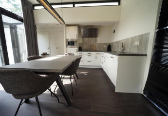 Moderne spise- og køkkenområde på L-Cube lodge i Spaarnwoude, Holland, med stilrent interiør og store vinduer.