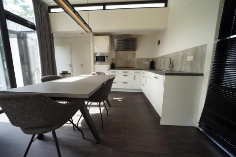 Moderne spise- og køkkenområde på L-Cube lodge i Spaarnwoude, Holland, med stilrent interiør og store vinduer.