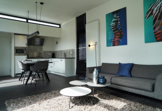 Soggiorno e cucina moderni nella L-Cube lodge a Spaarnwoude, Paesi Bassi, con arredi eleganti e opere d’arte.