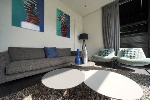 Woonkamer in L-Cube Spaarnwoude, Nederland met moderne banken, tafels en geometrische kunst aan de muur.
