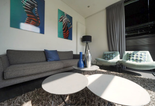 Woonkamer in L-Cube Spaarnwoude, Nederland met moderne banken, tafels en geometrische kunst aan de muur.