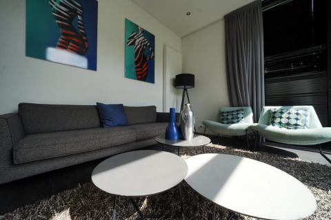Woonkamer in L-Cube Spaarnwoude, Nederland met moderne banken, tafels en geometrische kunst aan de muur.