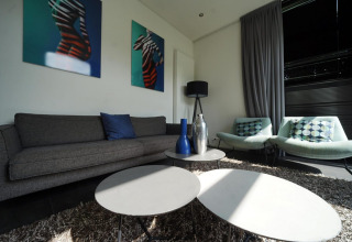 Sala de estar en L-Cube Spaarnwoude, Países Bajos, con sofás modernos, mesas y arte geométrico en la pared.