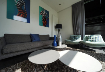 Stue i L-Cube Spaarnwoude, Nederlandene, med moderne sofaer, bord, farverige puder og abstrakt kunst.